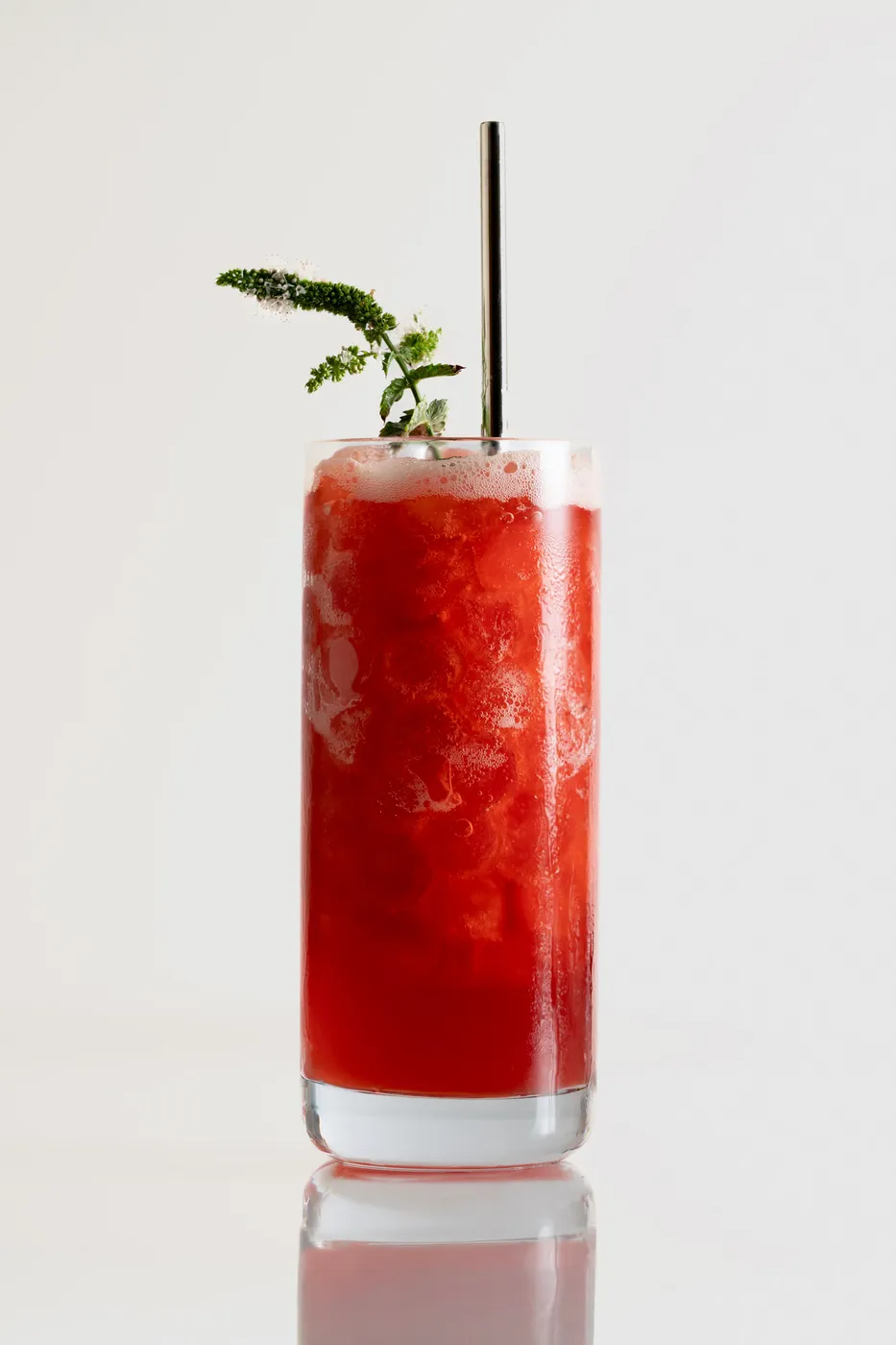 A bright red, sparkling cocktail with a mint flower garnish.