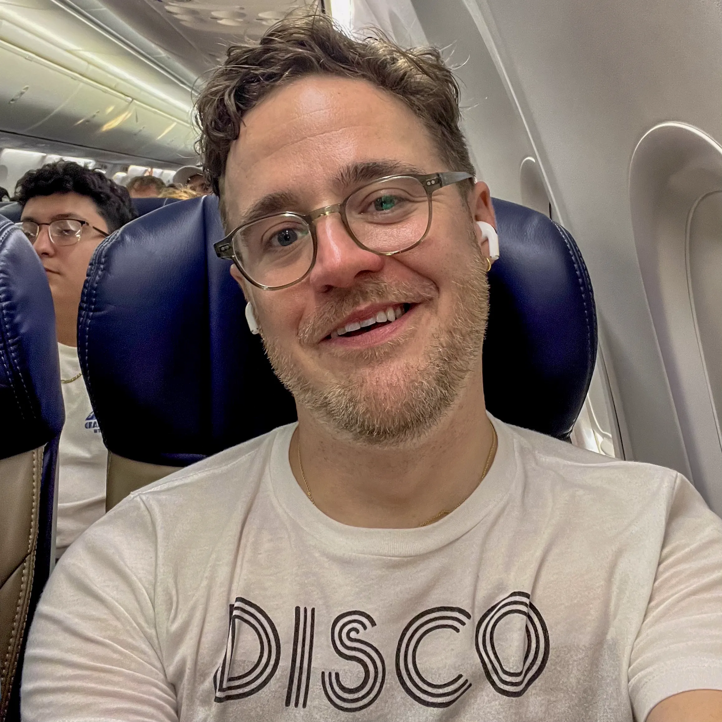 Clint smiling on an airplane, wearing a shirt that says DISCO.